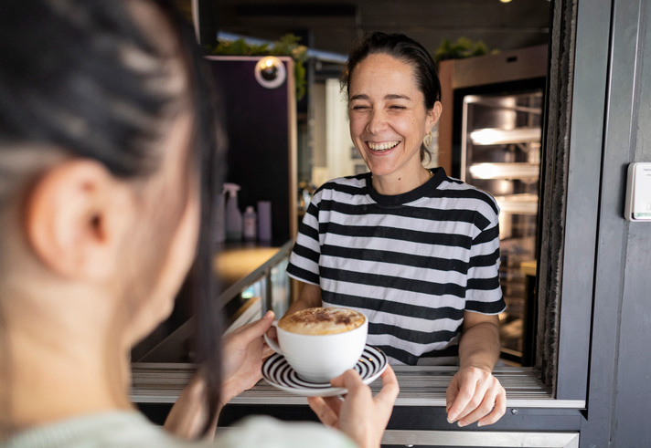 A woman hands a customer a cup of coffee from a serving window